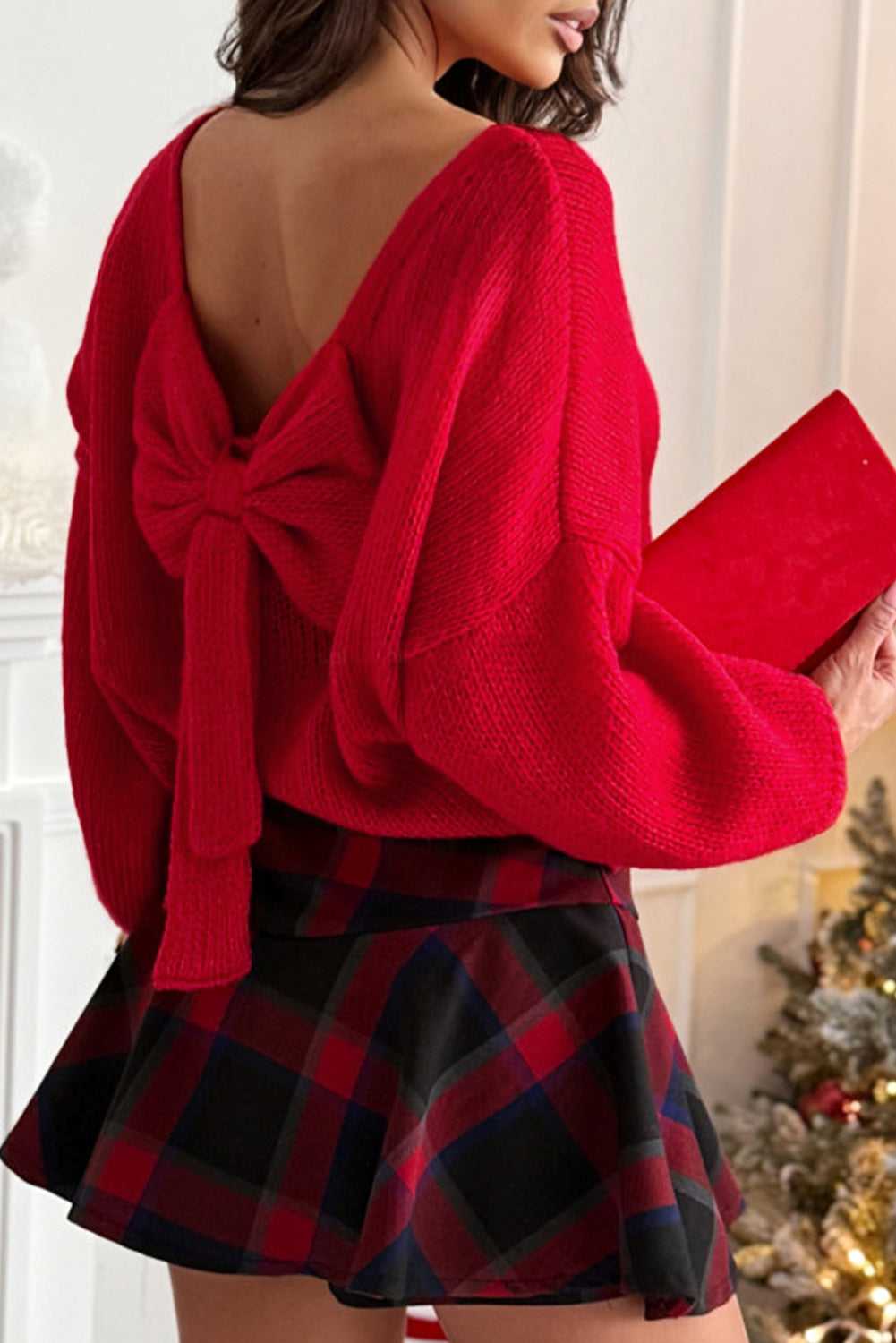 Red Women's Festive Bow‑Back Backless Jumper with large bow detail, styled with plaid skirt for a bold holiday outfit.
