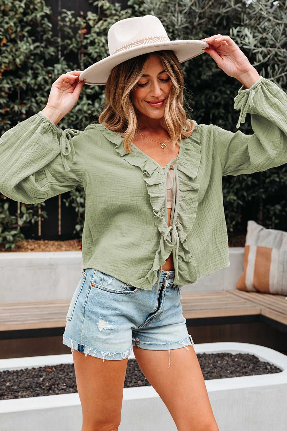 Model wearing Meadow Cotton Blouse - Soft & Lightweight | FashionFitz with wide sleeves and bow cuffs, styled with a hat and denim shorts.