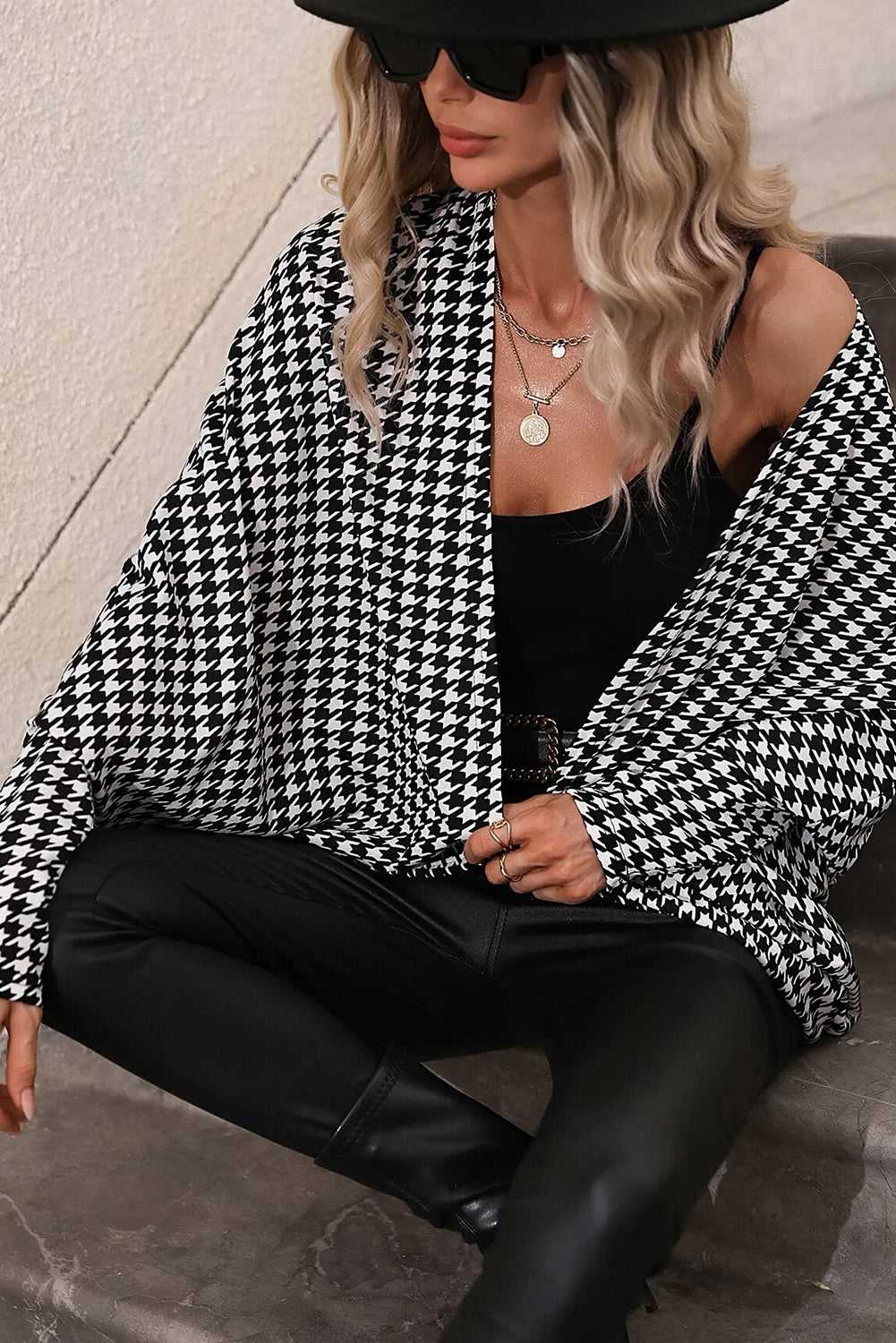 Person wearing a black and white houndstooth patterned jacket over a black top and pants.