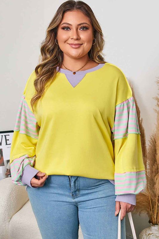 Plus size yellow sweatshirt with lilac and striped sleeves, styled casually with jeans for a cozy fall look.