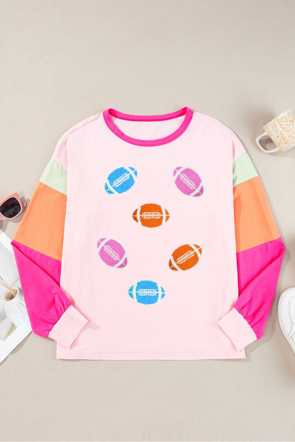Flat lay of Pink GAME DAY Graphic Top with colorful football graphics and color block long sleeves, ideal for sporty casual outfits.