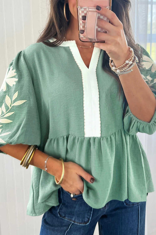 Women's smoke green embroidered sleeve tiered blouse with V-neckline and puff sleeves, styled with denim jeans for a casual chic look.