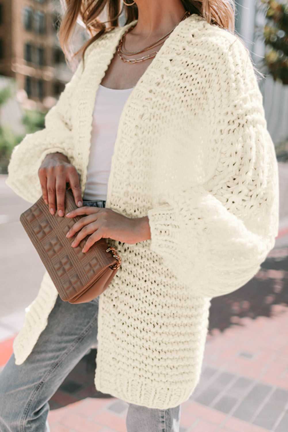 Close-up of cozy white oversized cardigan with textured chunky knit and balloon sleeves, styled with casual accessories.