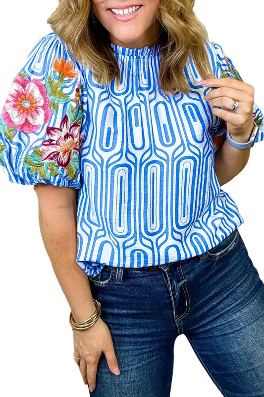 Woman wearing a blue patterned top with floral sleeves against a blurred background