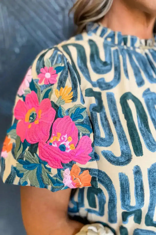 Close-up of puff sleeve on women's embroidered top, showing detailed pink and orange floral embroidery on lightweight fabric.