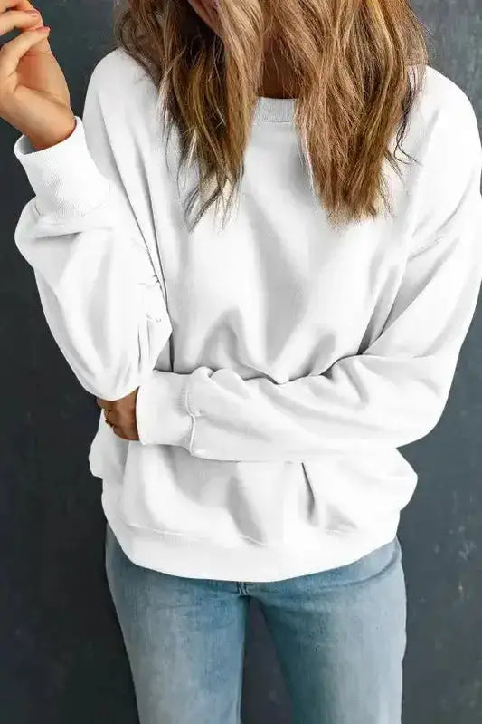 White classic crewneck sweatshirt with relaxed fit, paired with jeans. Ideal for layering in cold weather and everyday comfort.