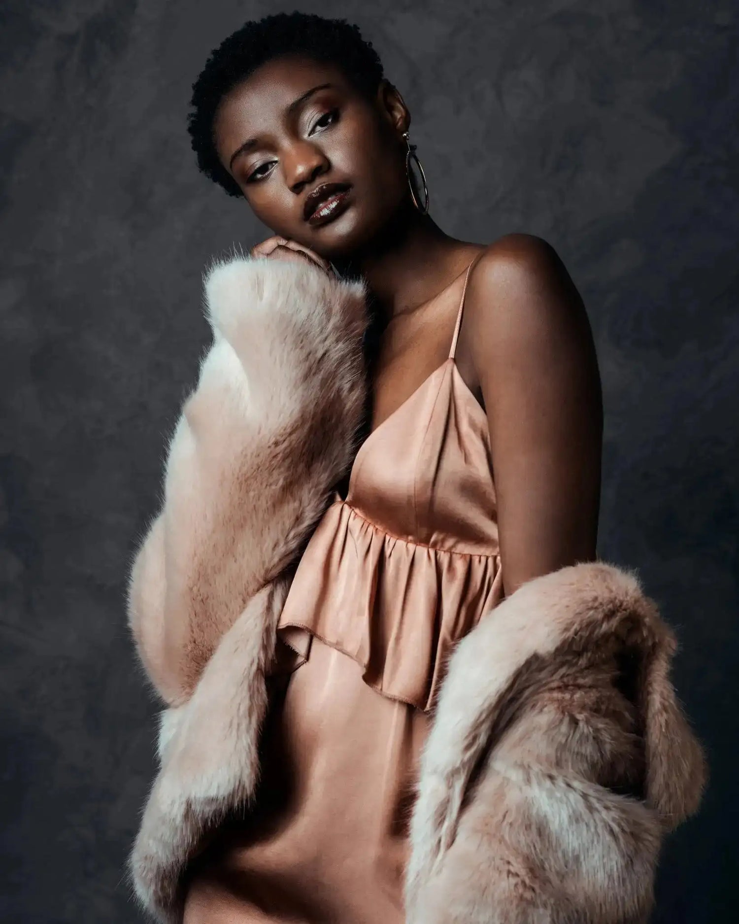 Woman wearing a pink satin dress and fur coat against a dark background