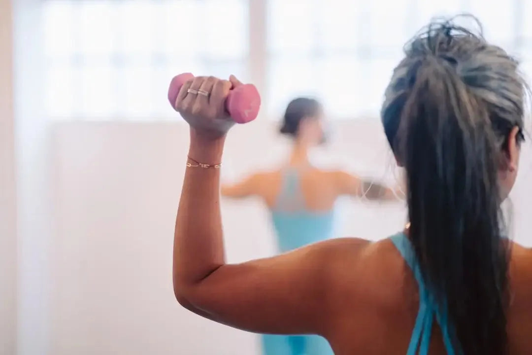 Woman exercising with a pink dumbbell while wearing a red sports bra and shorts set in a gym