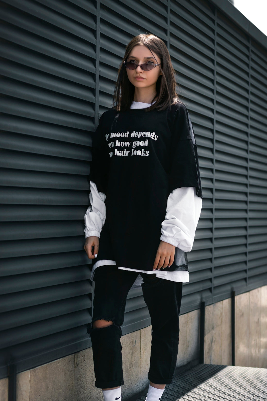a woman standing against a wall wearing a sweatshirt and ripped jeans