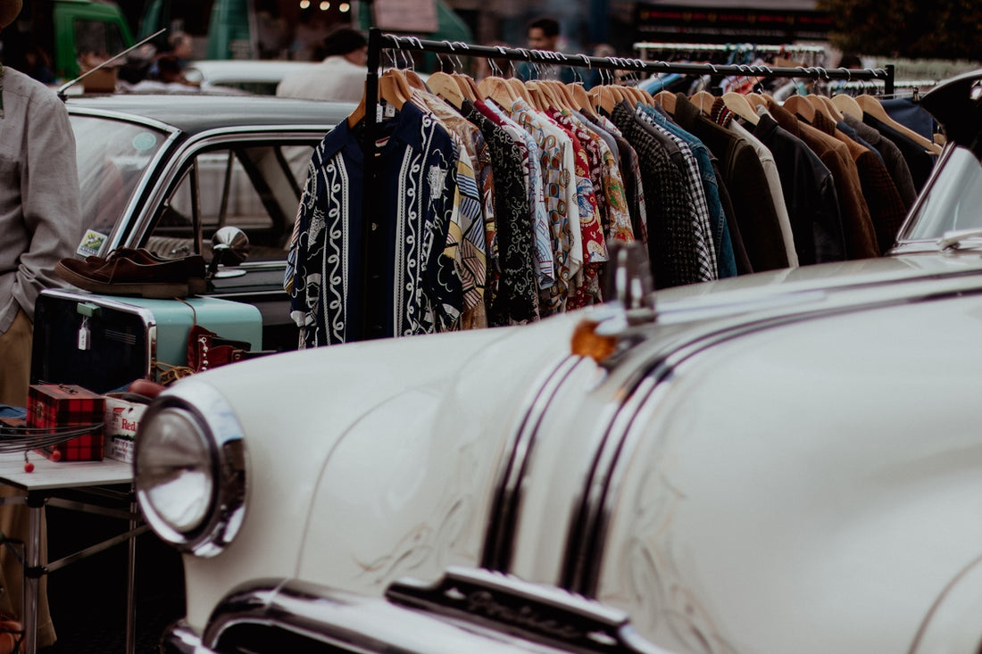 a man standing next to a white car in front of a row of shirts