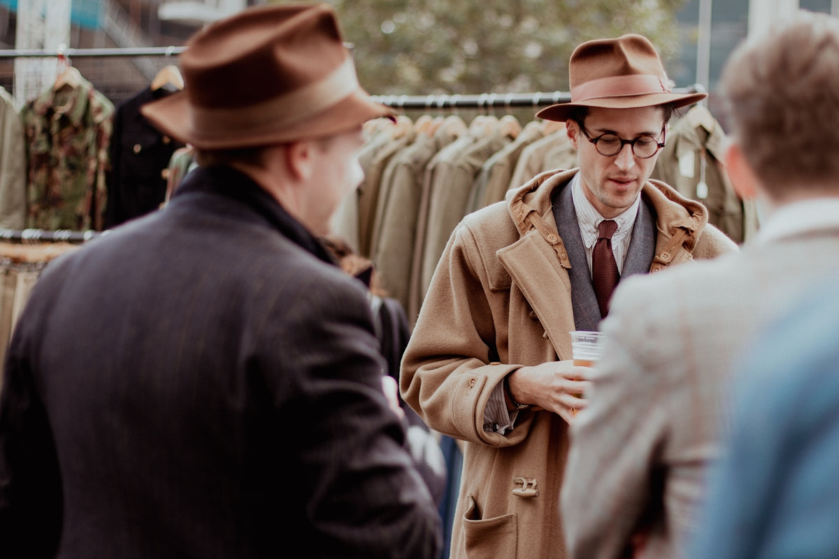 a man in a coat and hat talking to another man