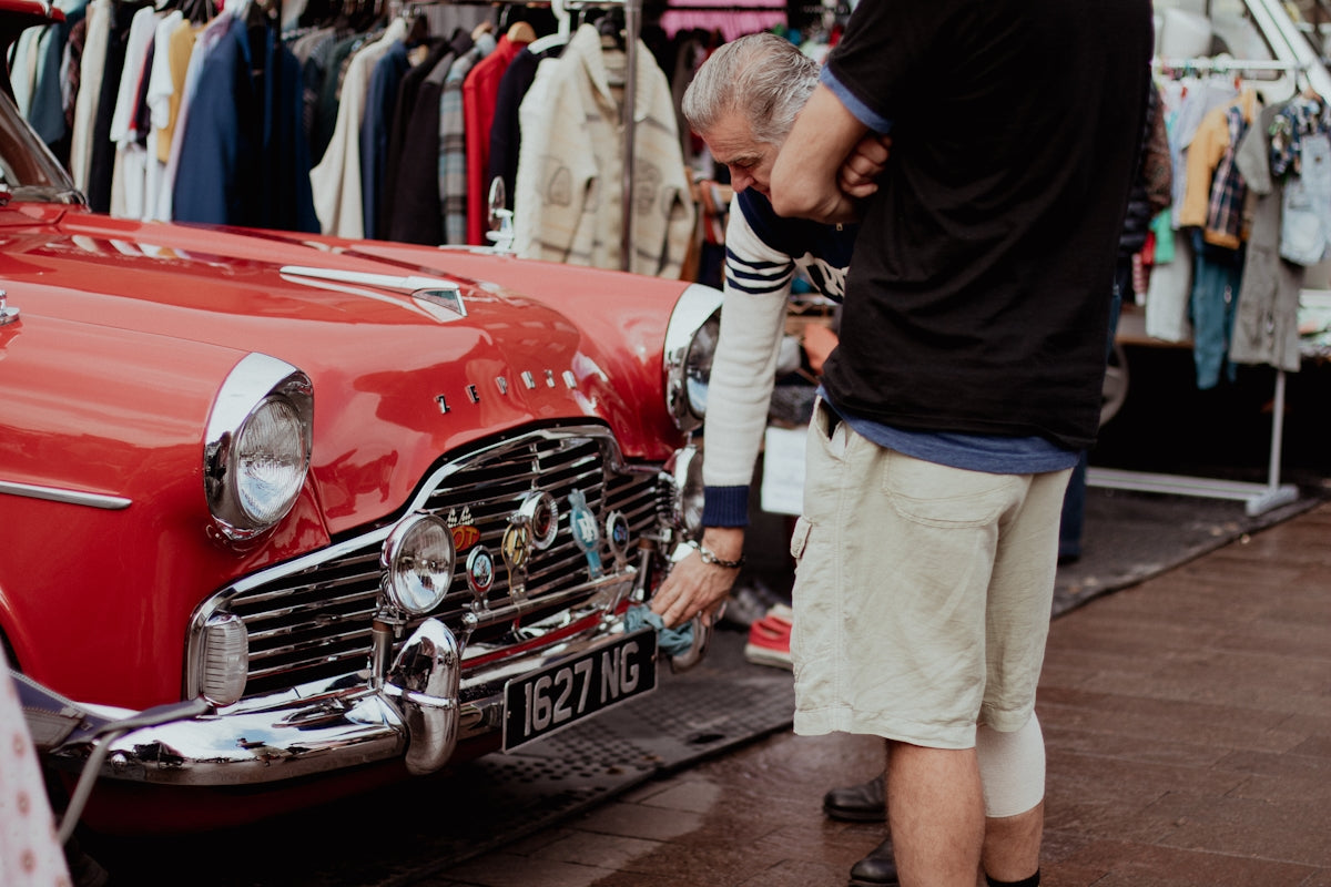 a man looking at an old red car