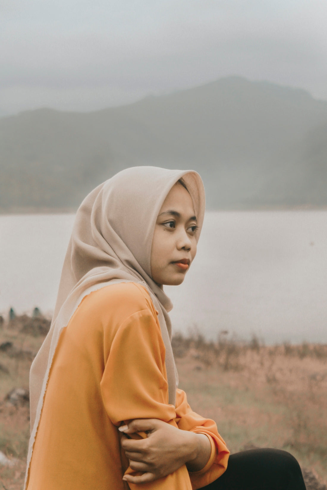 a woman sitting on top of a rock next to a body of water