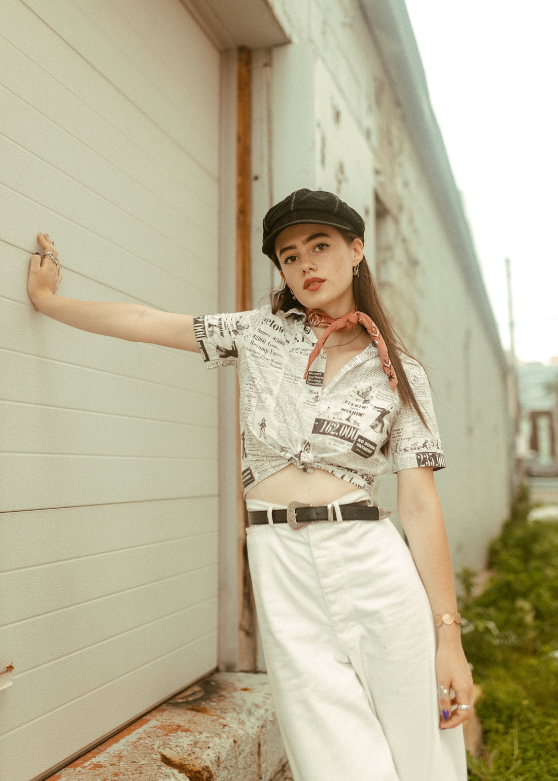 a woman leaning against a wall wearing a hat