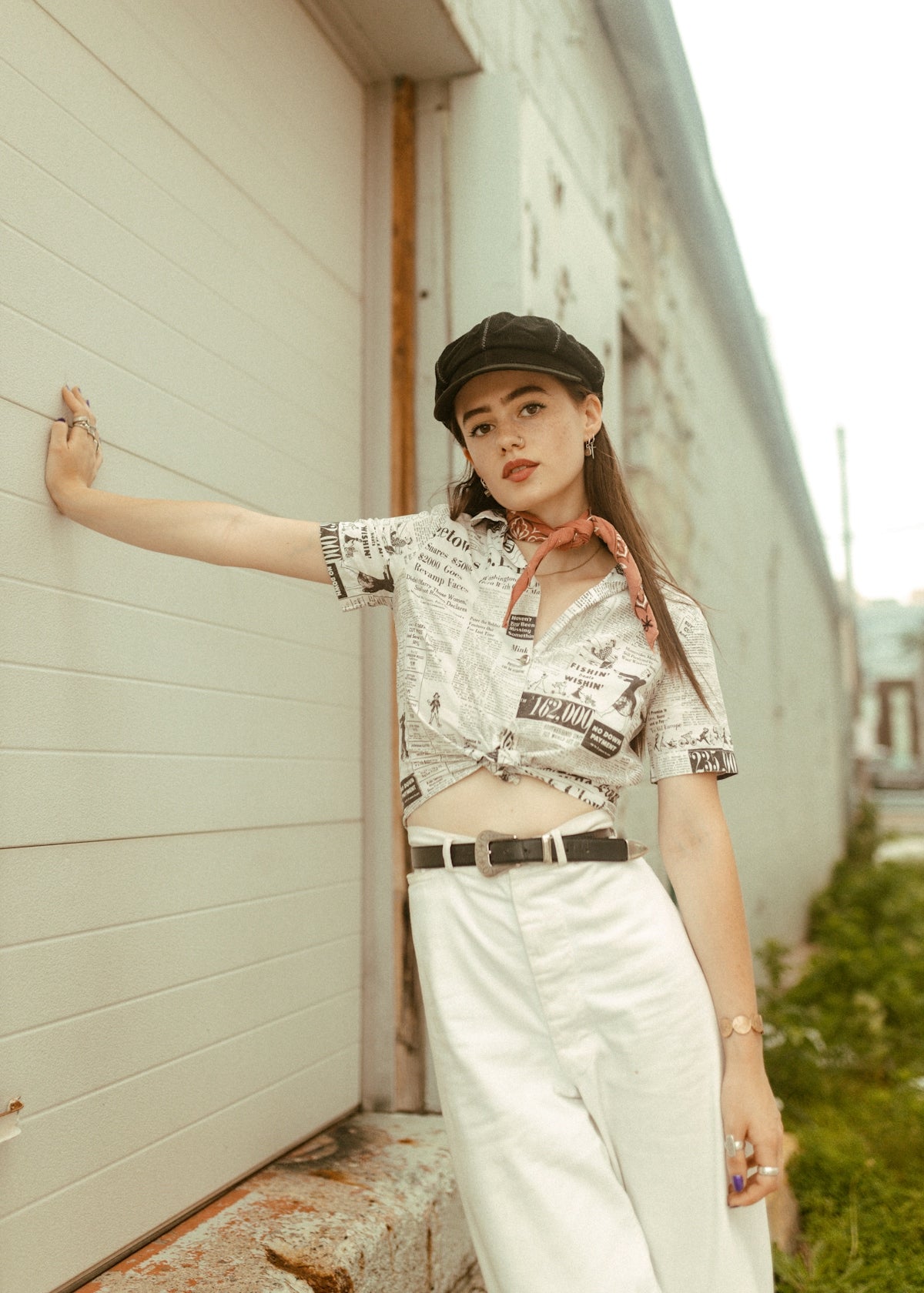 a woman leaning against a wall wearing a hat