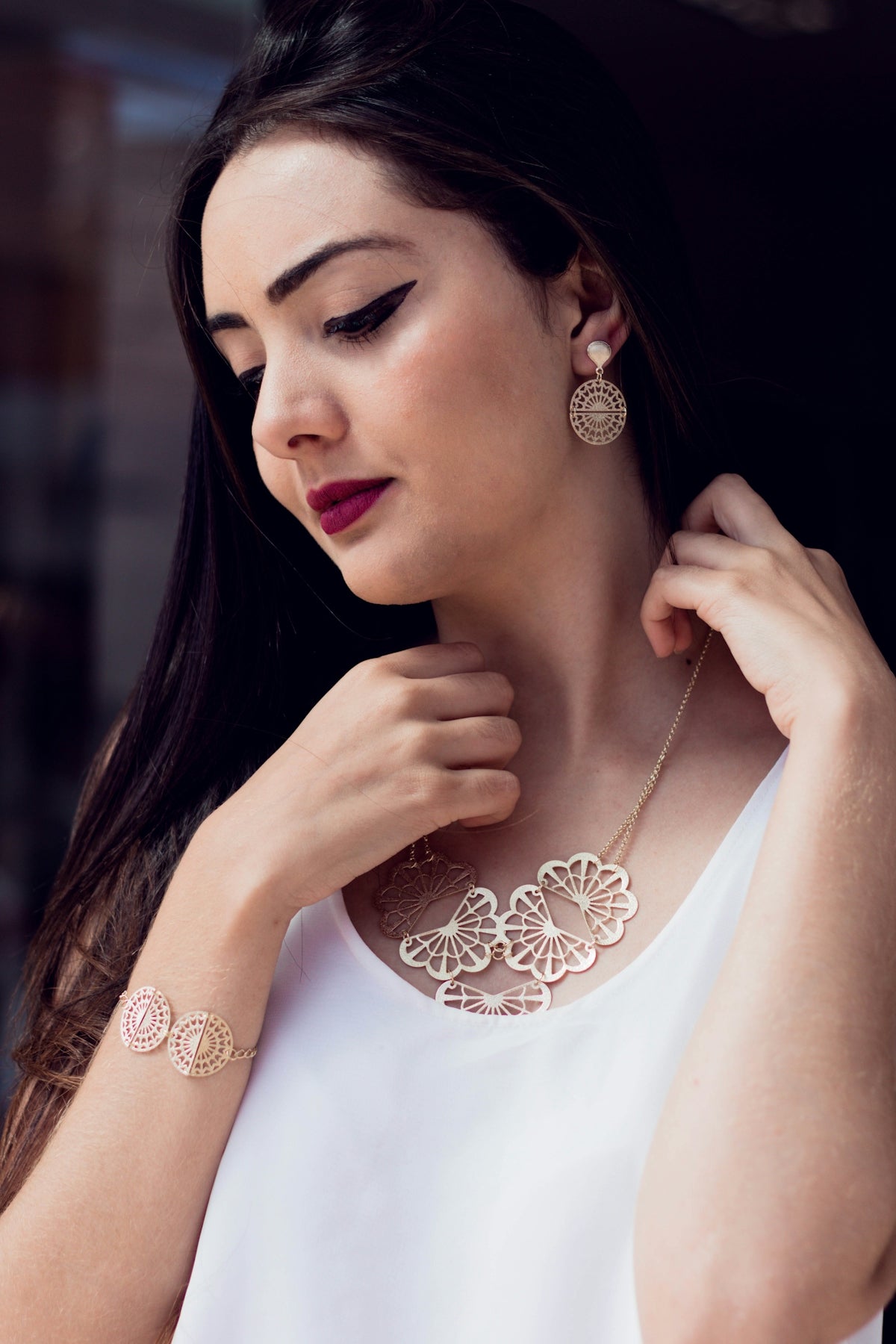 A woman in a white top is wearing a necklace and earrings