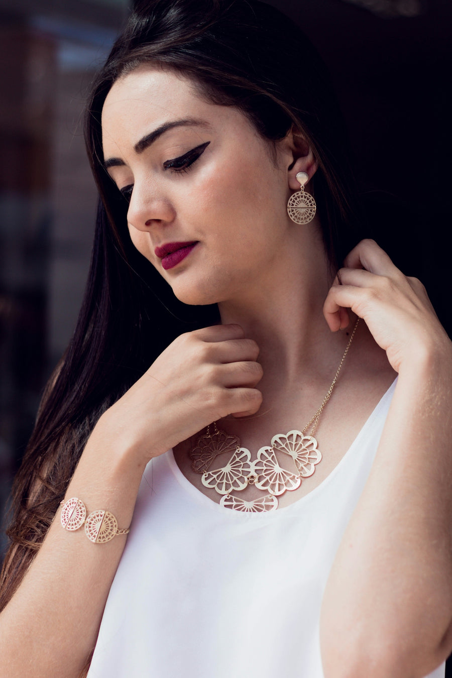 A woman in a white top is wearing a necklace and earrings