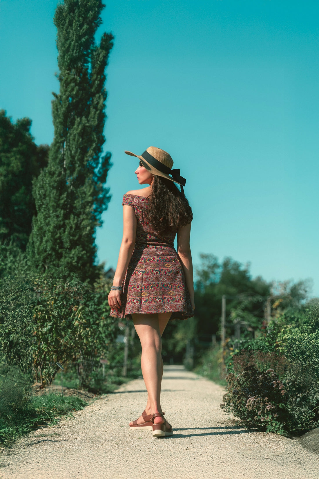 Woman in a dress and hat walking on a path.