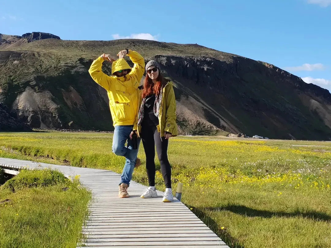 Couple wearing stylish waxed jackets posing on a wooden path in a scenic landscape