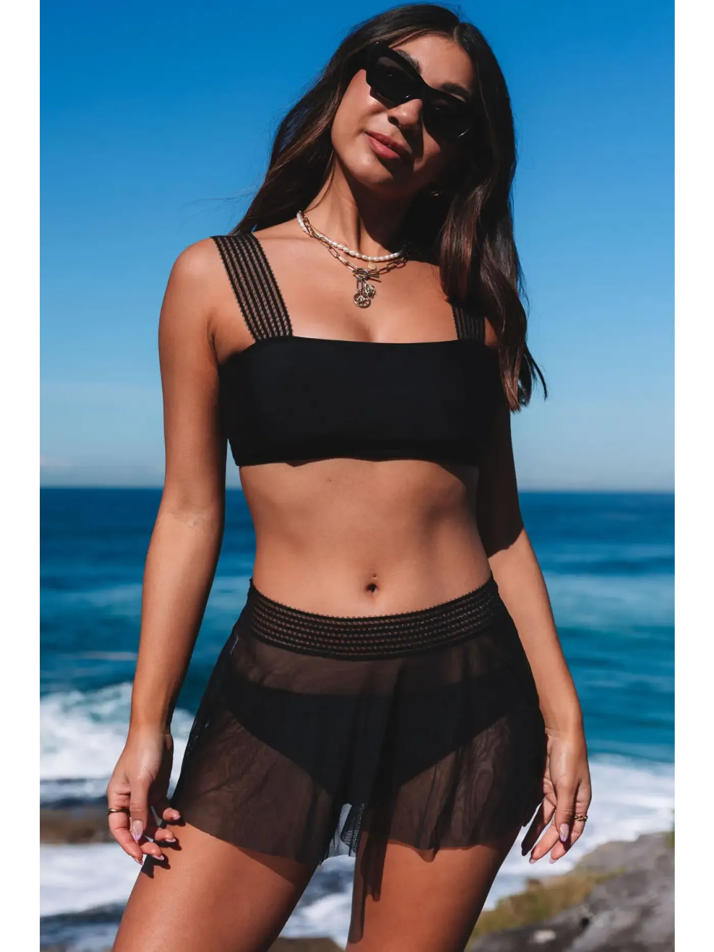 Trendy Bikinis Collection showcasing a model in a black bikini set against a beach backdrop