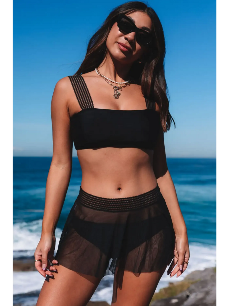 Trendy Bikinis Collection showcasing a model in a black bikini set against a beach backdrop