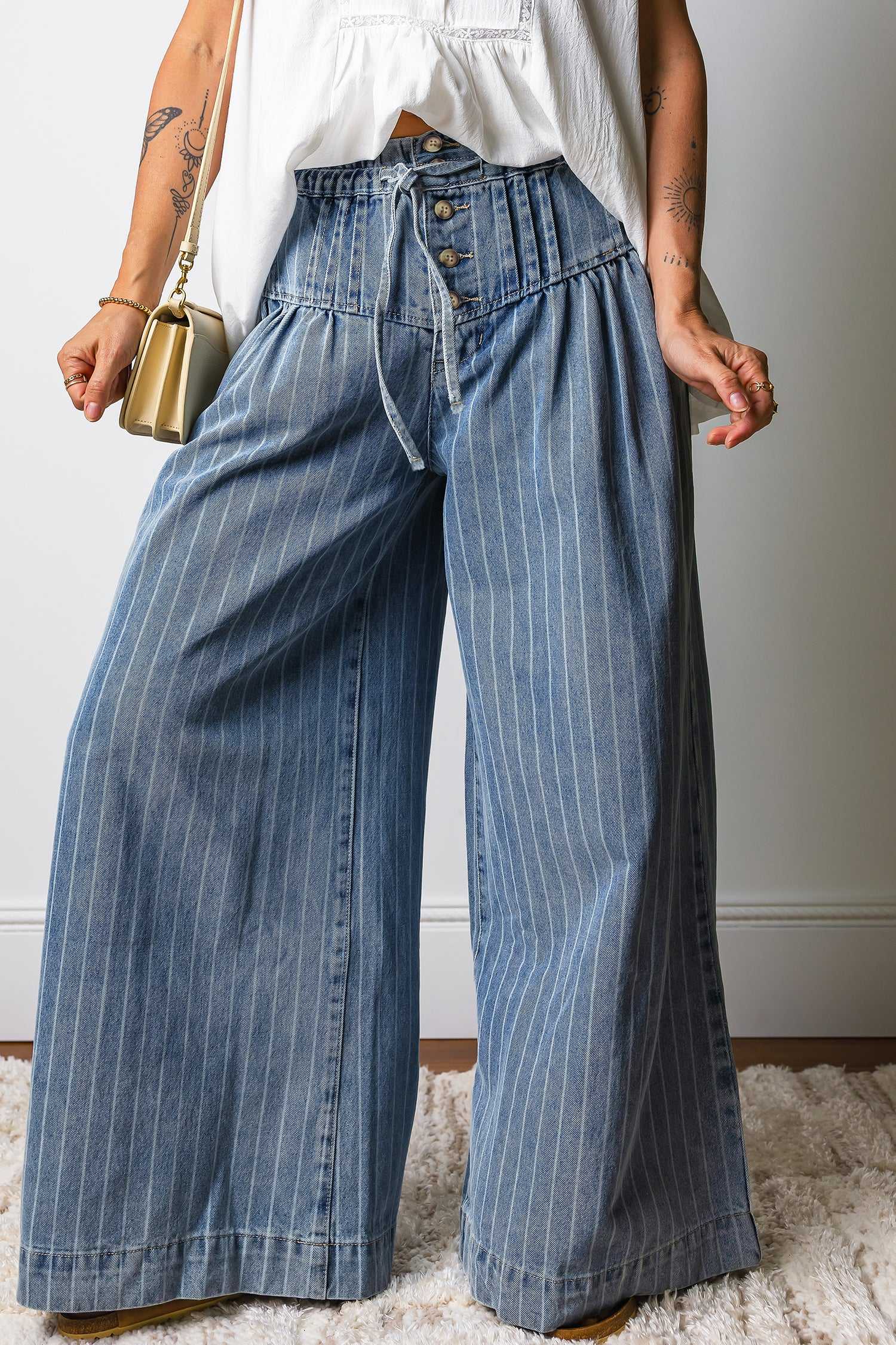 Front view of relaxed fit pinstripe drawstring jeans with button fly and pleated waist, designed for everyday wear and fashion-forward outfits.