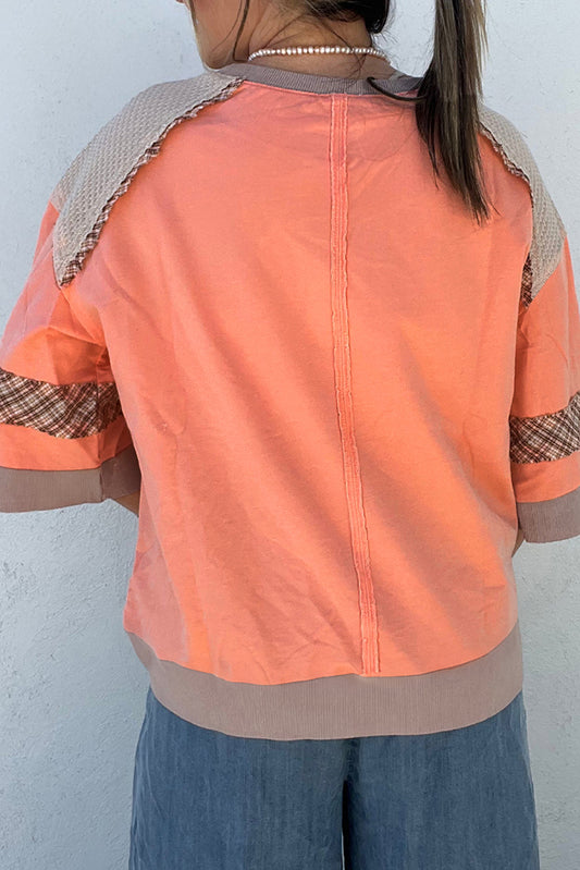 Person wearing an orange shirt with patterned sleeves against a light blue background