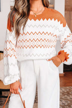 Person wearing a white and orange patterned sweater with white pants indoors.