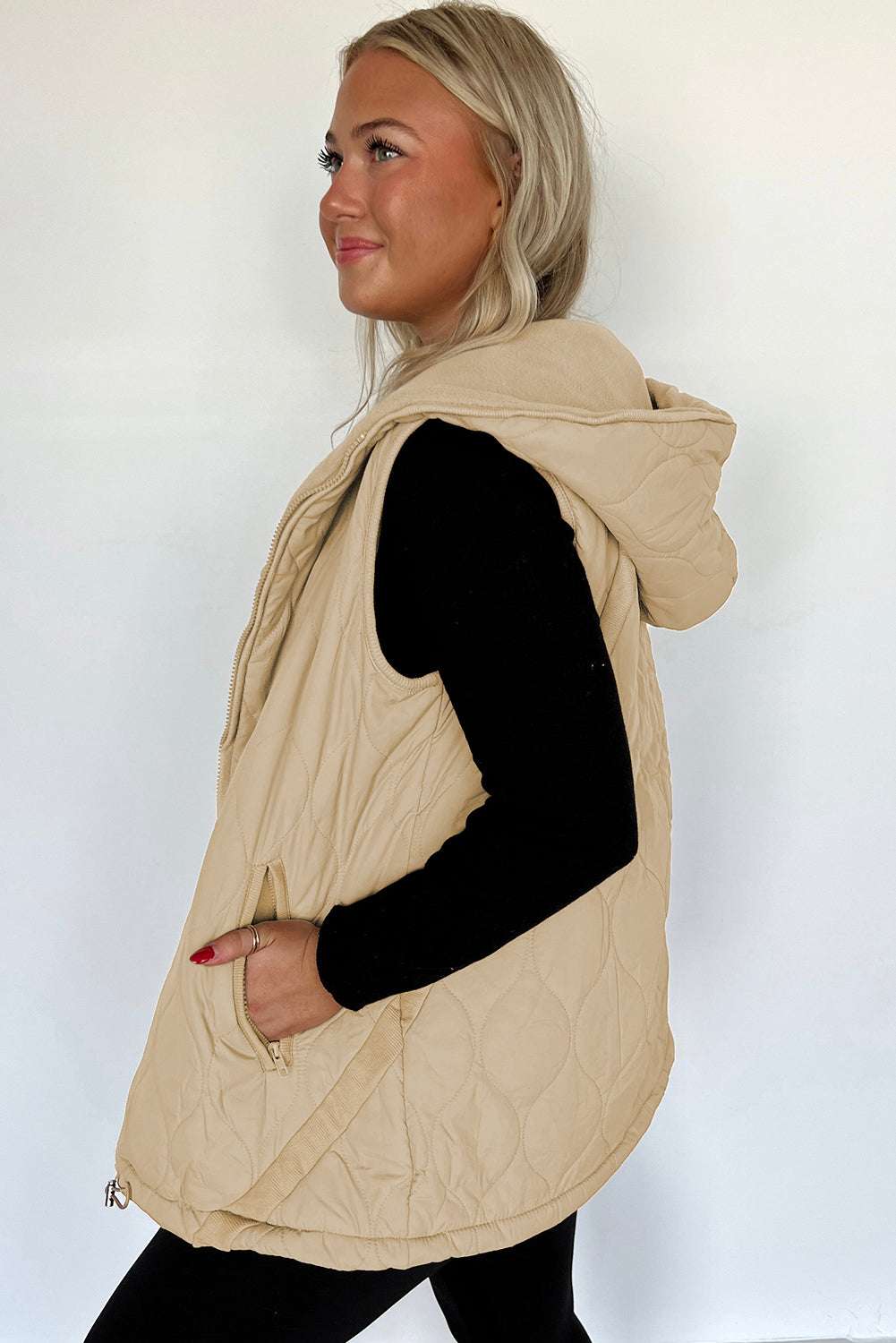 Side view of khaki Quilted Fleece‑Lined Winter Gilet with hood and curved hem, styled casually over black clothing.