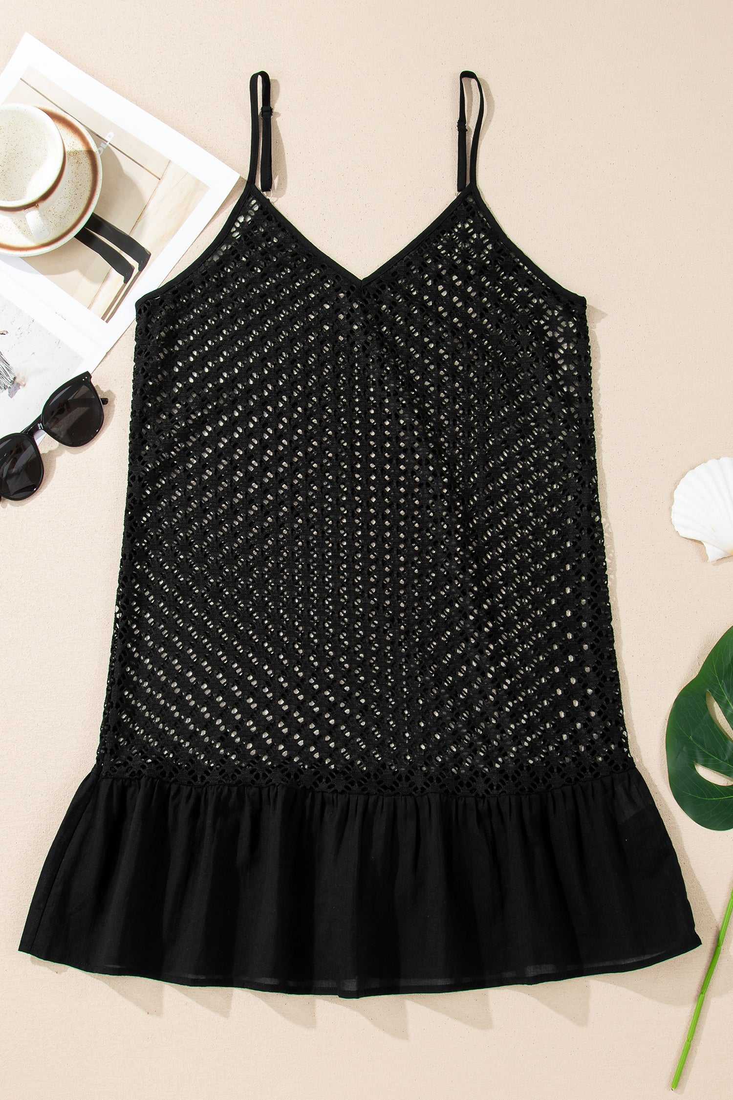 Flat lay of black crochet beach cover-up on beige surface