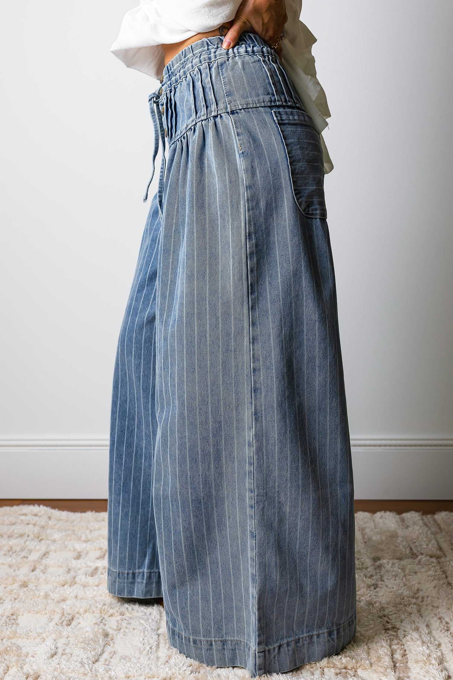 Side profile of women's baggy pinstripe jeans with wide leg silhouette and drawstring waist, offering a trendy and comfortable fit.