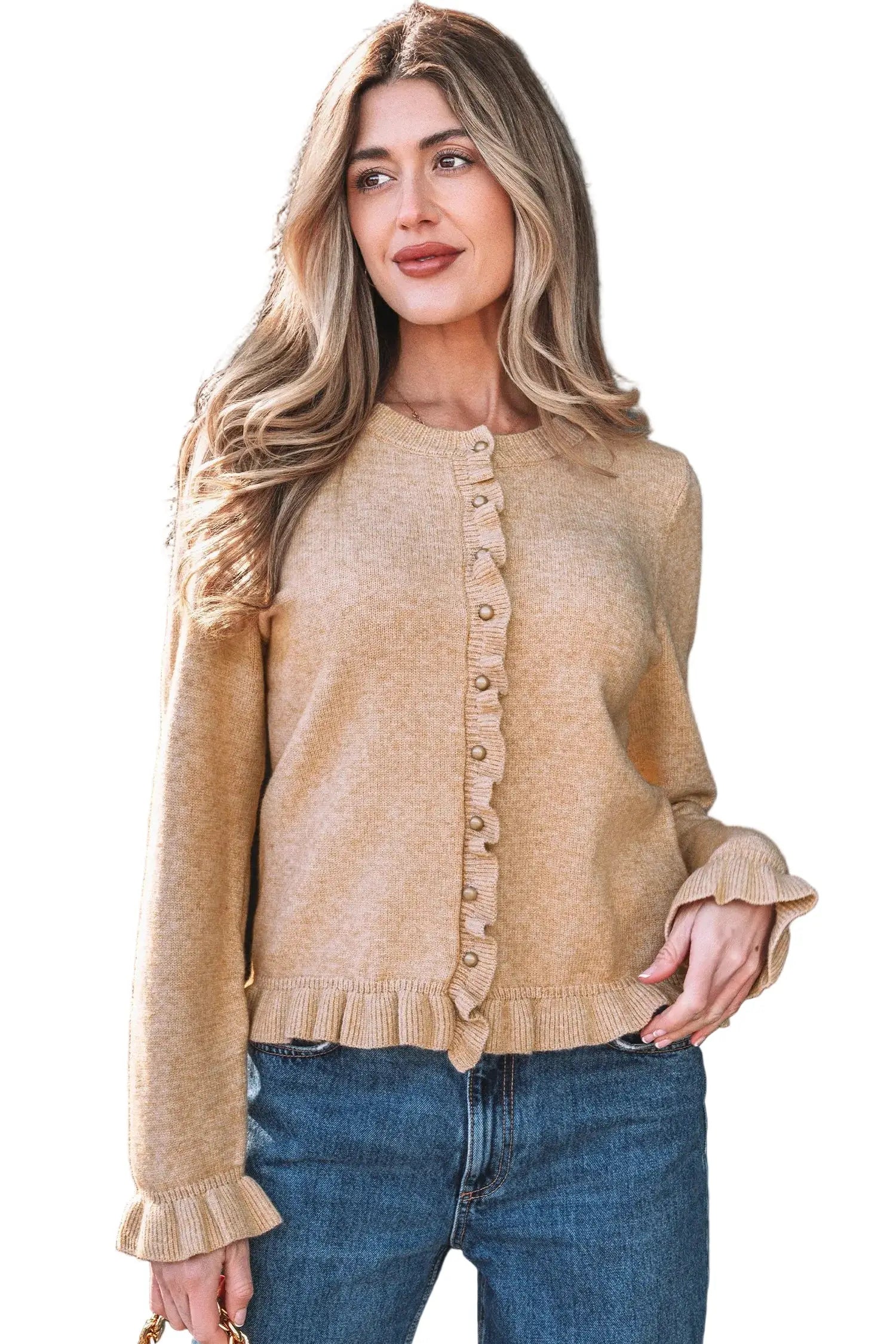Woman wearing a beige cardigan and blue jeans against a black background