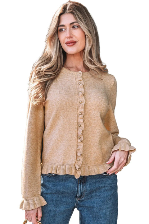 Woman wearing a beige cardigan and blue jeans against a black background