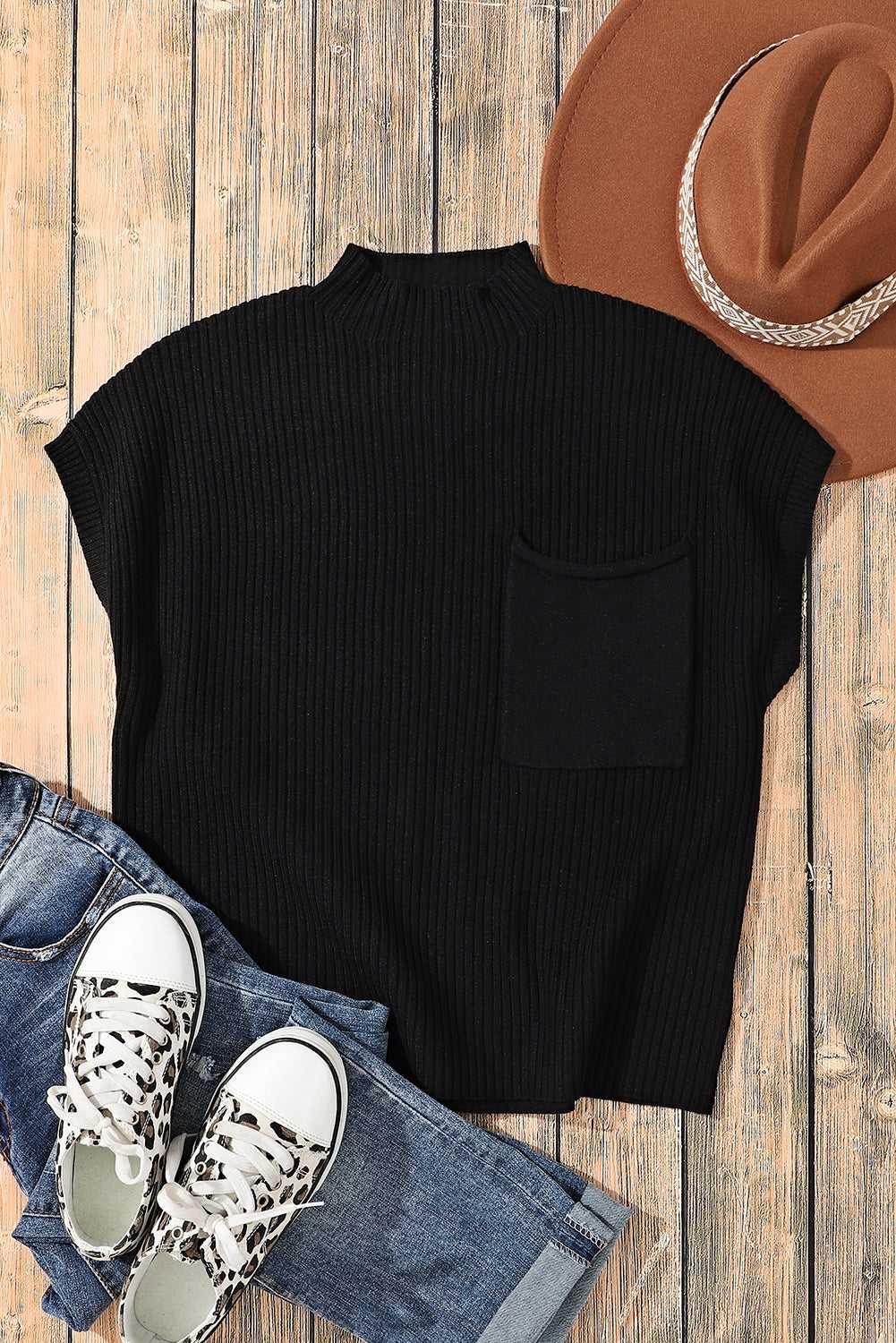 Flat lay of black ribbed knit top with chest pocket, paired with jeans, sneakers, and a hat for casual winter styling.