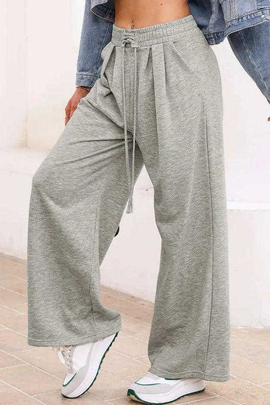 Gray pleated sweatpants with wide legs and drawstring waist, styled with sneakers for a relaxed autumn look.