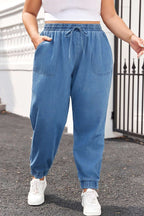 Plus Size Blue Denim Joggers with Drawstring Waist styled with white sneakers, featuring front pockets and elastic cuffs for casual wear.