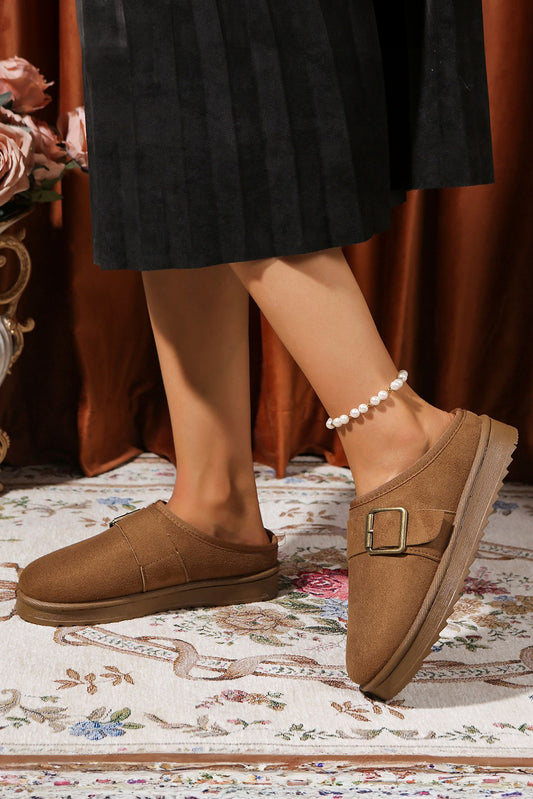 Brown vegan suede clog slippers worn on a patterned rug with a blurred background