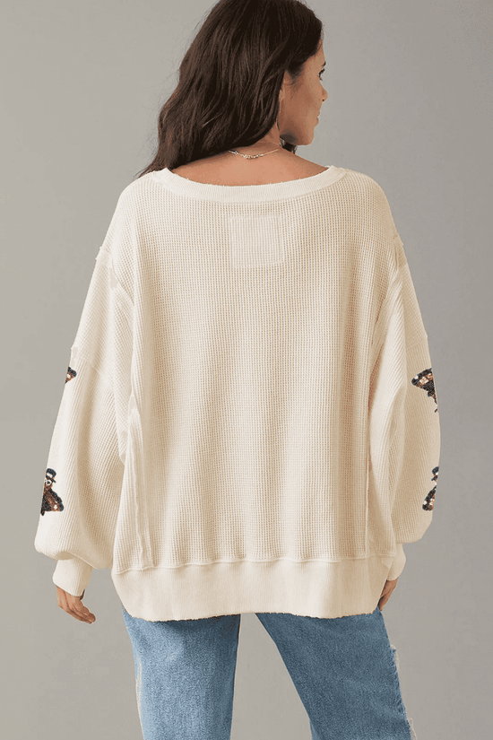 Woman wearing a cream sweater with lace sleeves against a gray background