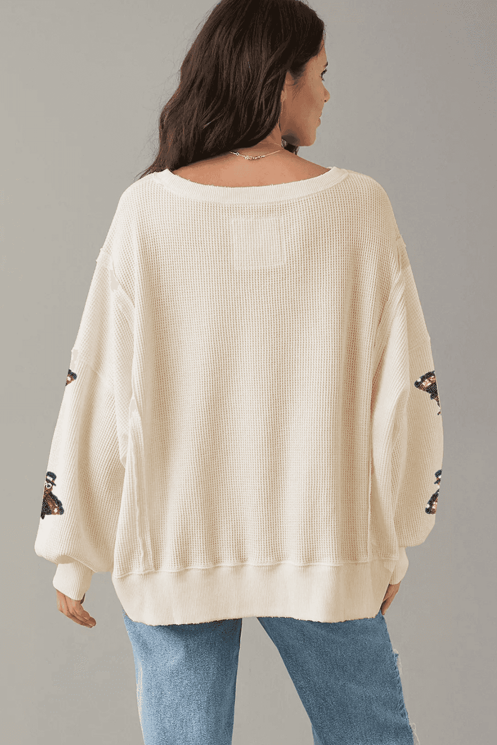 Woman wearing a cream sweater with lace sleeves against a gray background