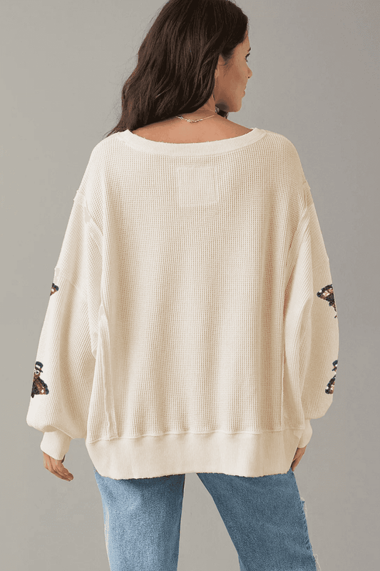 Woman wearing a cream sweater with lace sleeves against a gray background