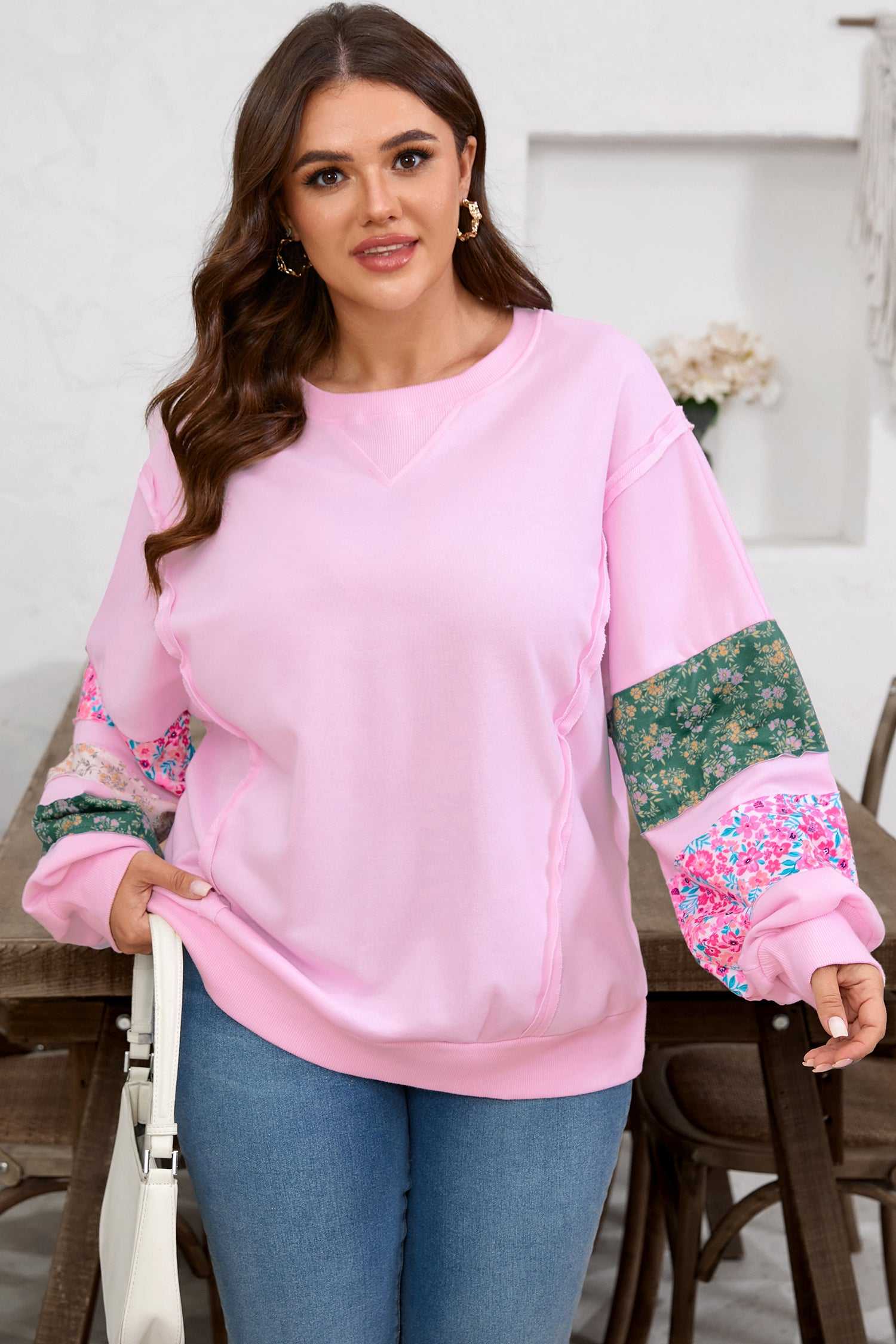 Curve Pink Floral Sleeve Baggy Sweatshirt for Women featuring soft pink fabric and colorful floral sleeves, paired with jeans and a white handbag.