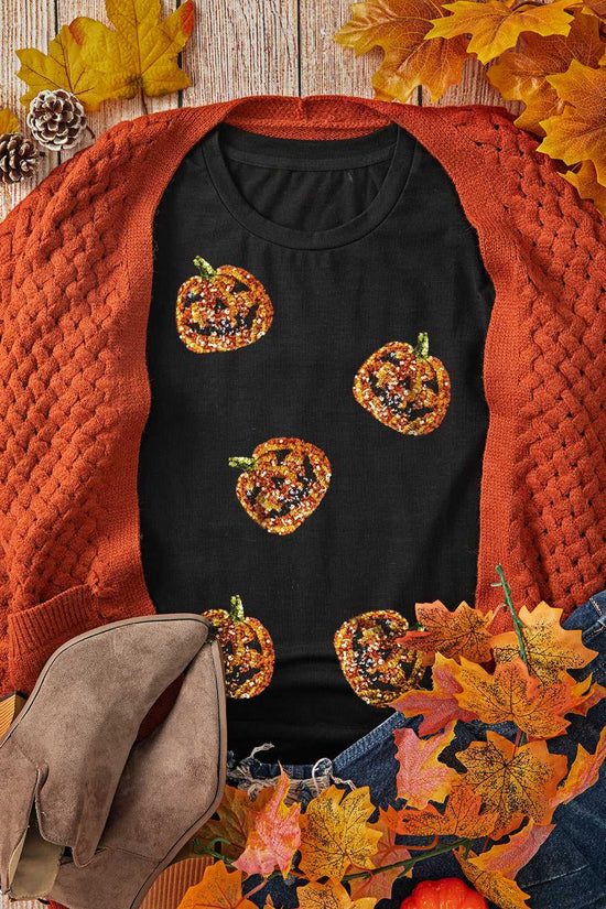 Black t-shirt with pumpkin designs worn over an orange sweater, surrounded by autumn leaves and pinecones.