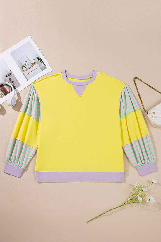Flat lay of plus size yellow sweatshirt with lilac trim and striped sleeves, showcasing its casual and colorful design.