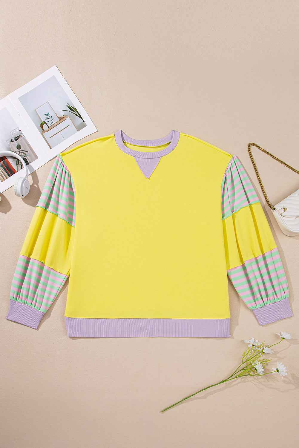 Flat lay of plus size yellow sweatshirt with lilac trim and striped sleeves, showcasing its casual and colorful design.