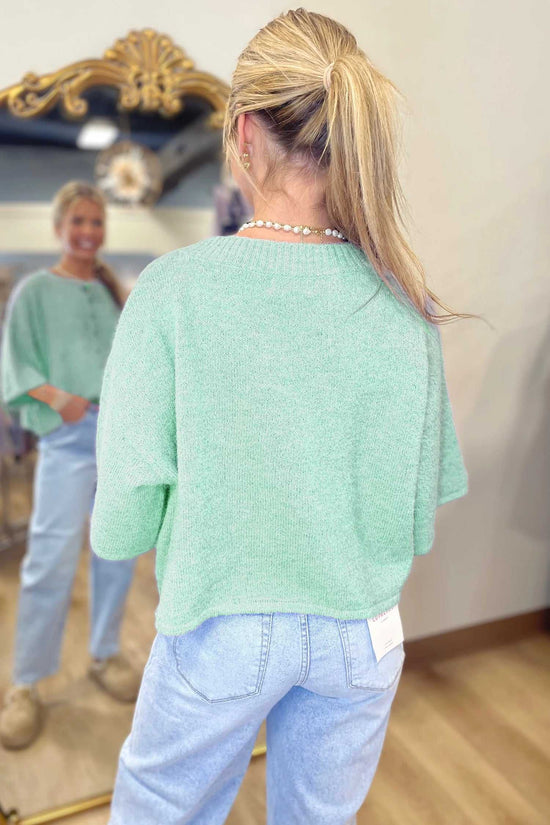 Back view of pastel jade fuzzy knit cardigan with relaxed boxy fit and short sleeves, styled with high-rise jeans.