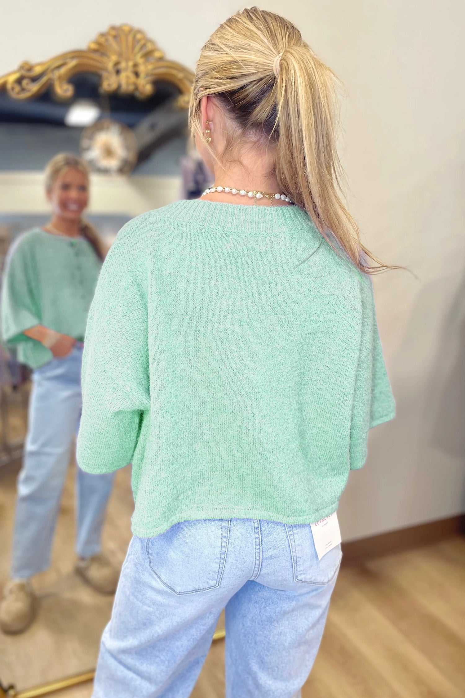 Back view of pastel jade fuzzy knit cardigan with relaxed boxy fit and short sleeves, styled with high-rise jeans.