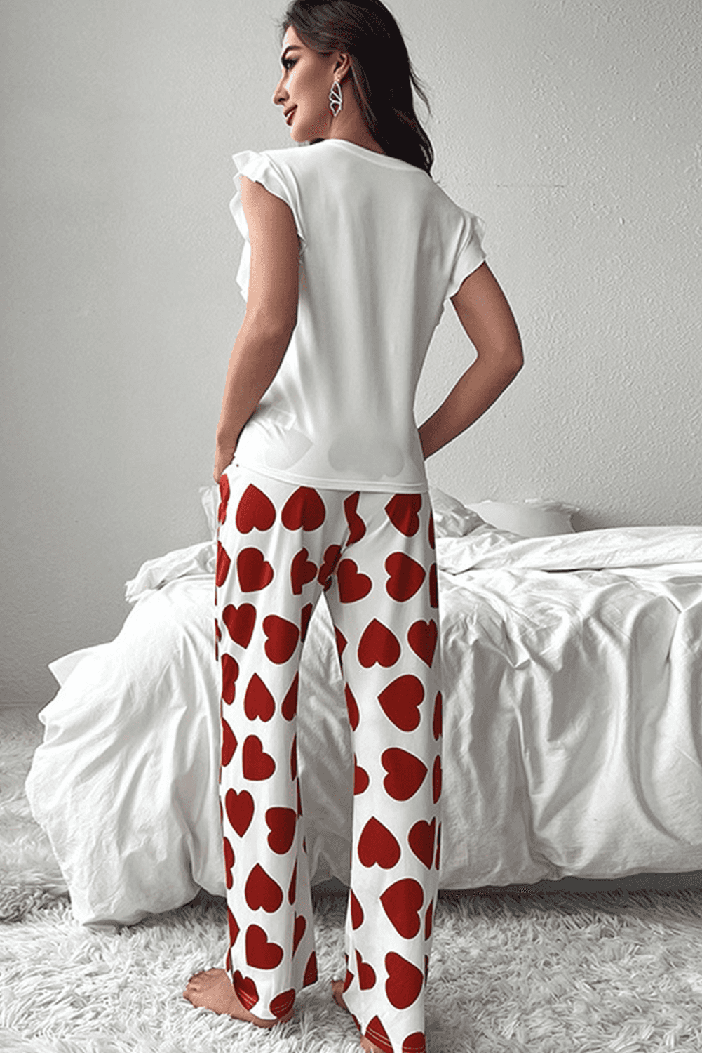 Woman wearing a white top and red heart-patterned pants in a bedroom setting.