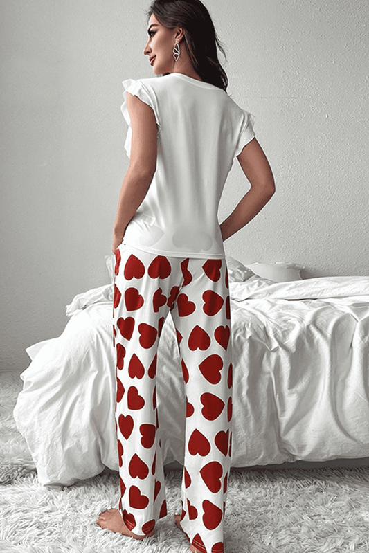 Woman wearing a white top and red heart-patterned pants in a bedroom setting.