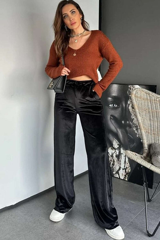 Model wearing black velvet straight-leg trousers with a rust knit top and accessories. Stylish women’s pants for seasonal elegance.