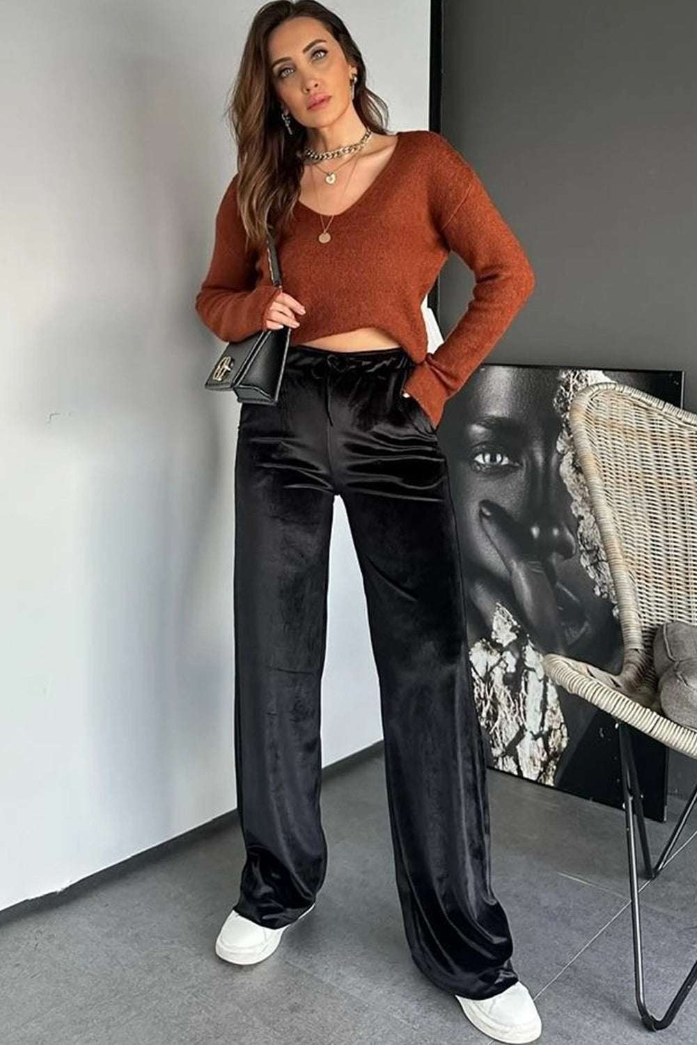 Model wearing black velvet straight-leg trousers with a rust knit top and accessories. Stylish women’s pants for seasonal elegance.
